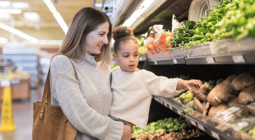 A mother and daughter select a vegetable from the produce section of a store